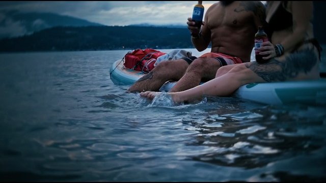 Two friends relaxing on a paddleboard with drinks on Shuswap Lake